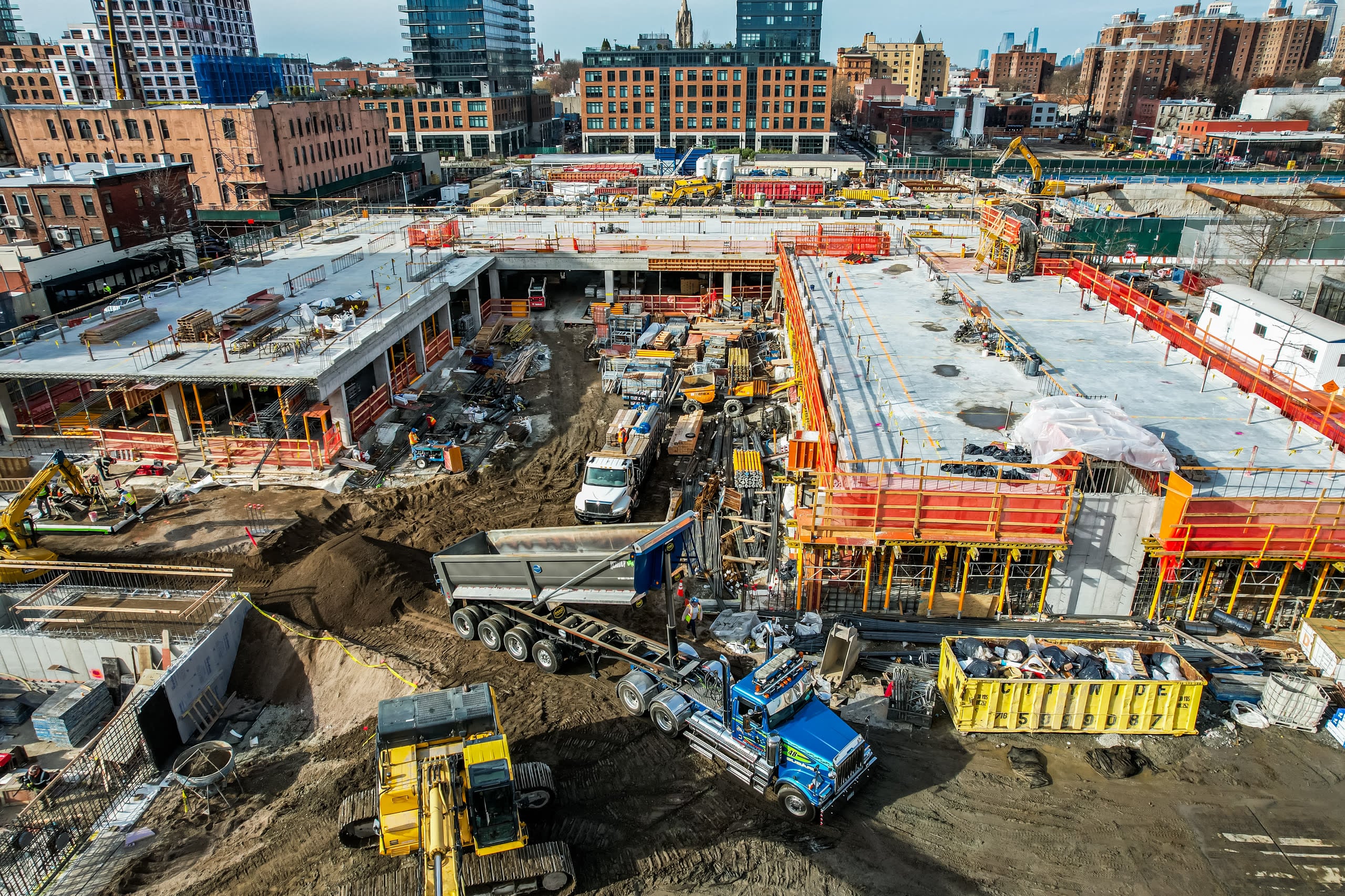 Winter aerial of a foundation-phase jobsite with excavators and delivery trucks