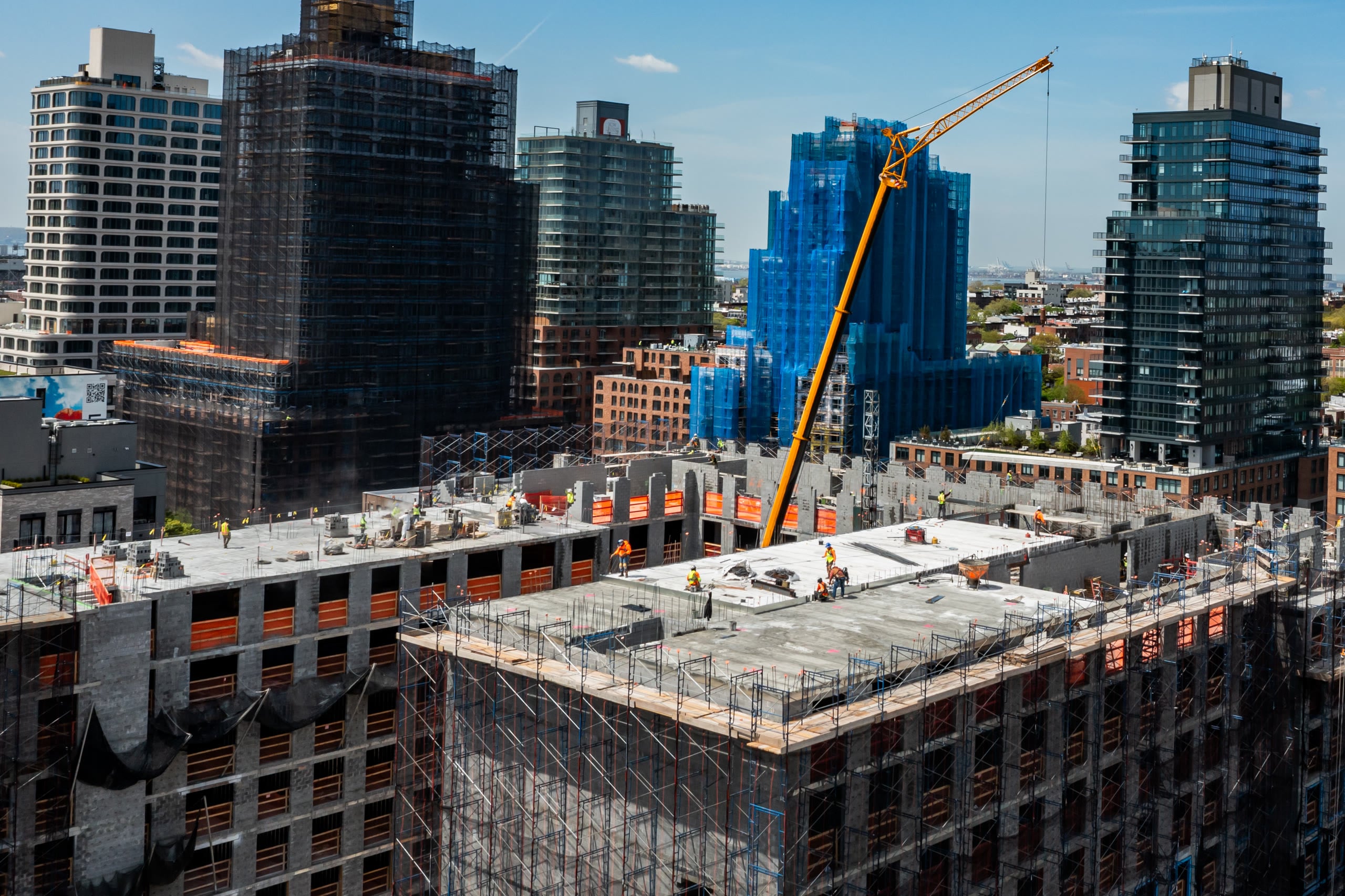 High aerial of a topped-out building with crews on deck and the city skyline behind
