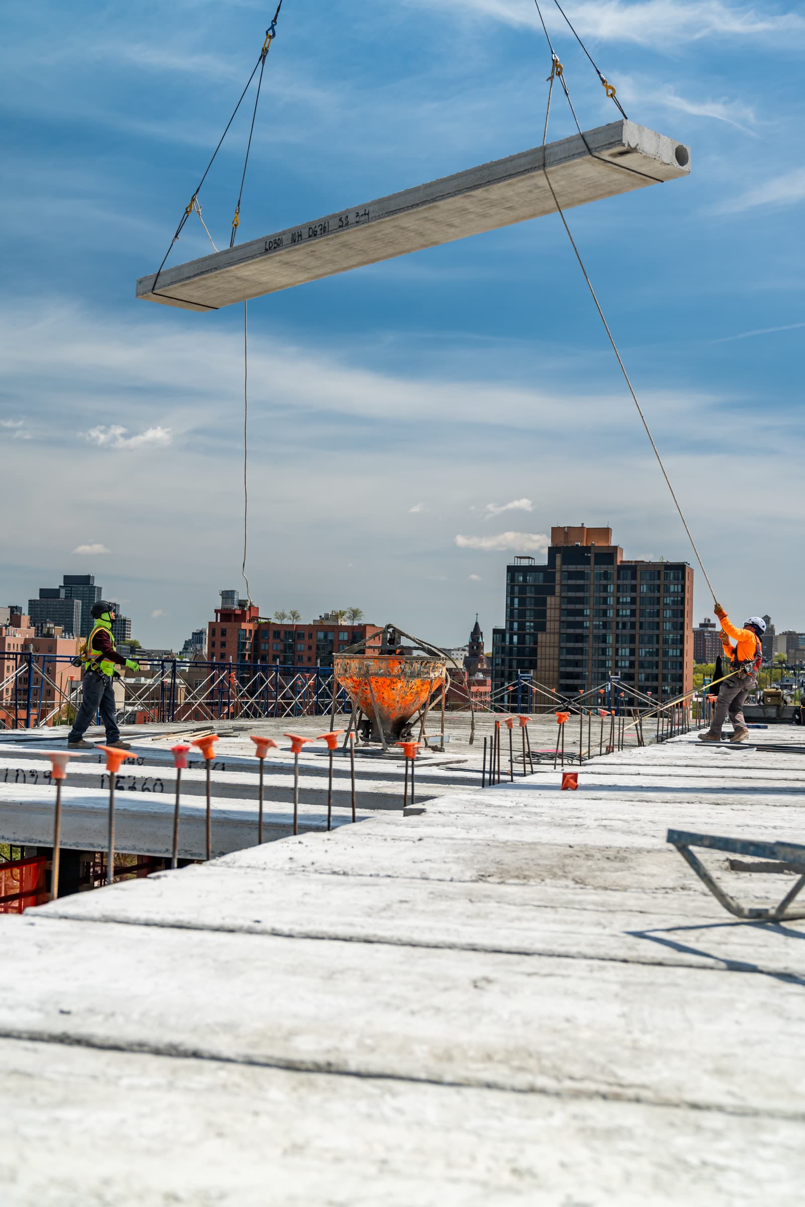 Hollow-core plank flying on crane rigging over a rooftop crew