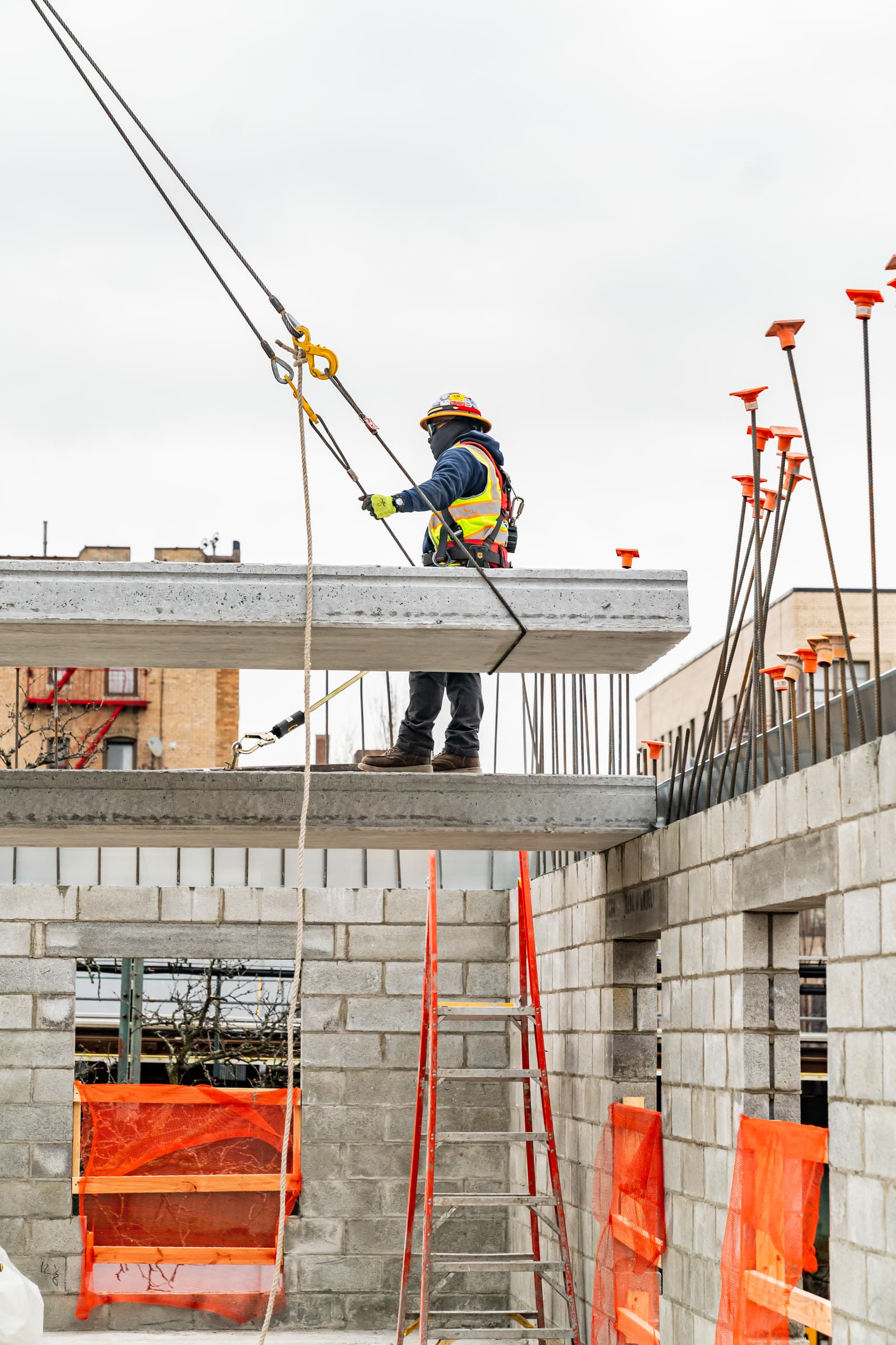 Harnessed worker tied off while guiding crane rigging at a plank leading edge