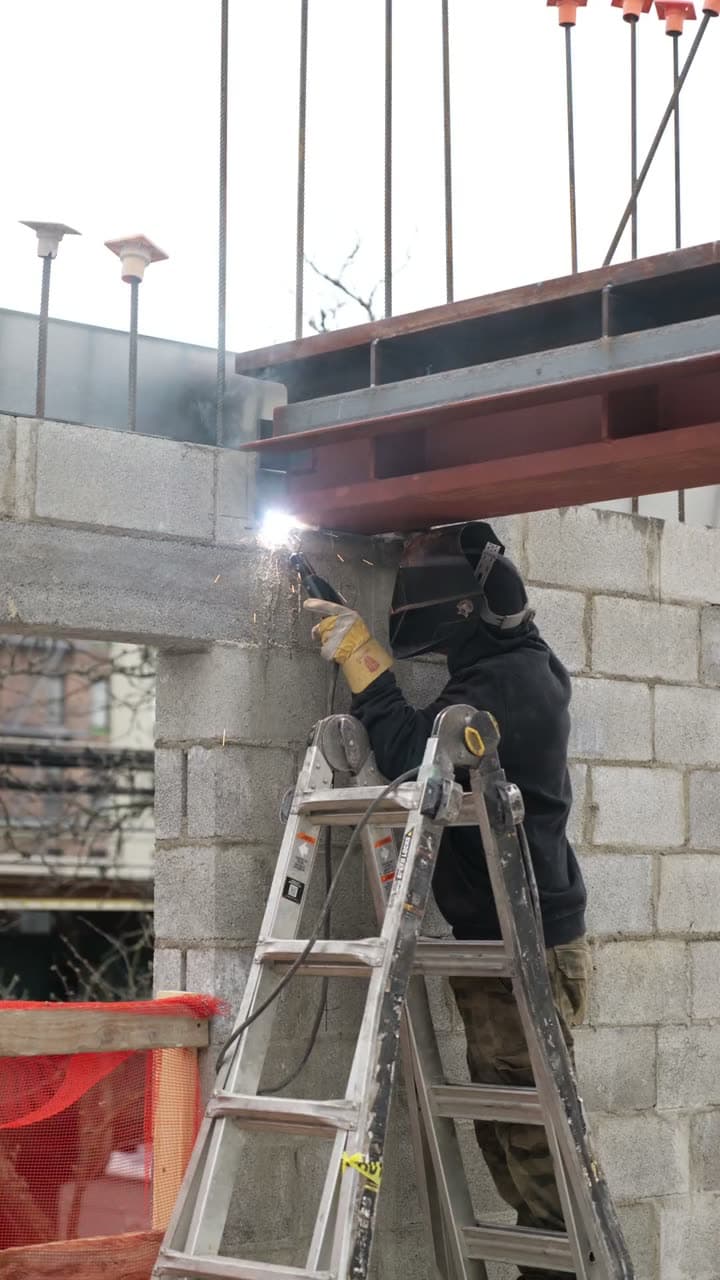 Metro Erectors welder working under a steel beam on a masonry building
