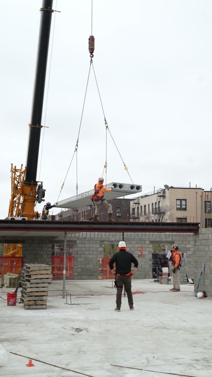 Hollow-core plank flying on crane rigging over a jobsite
